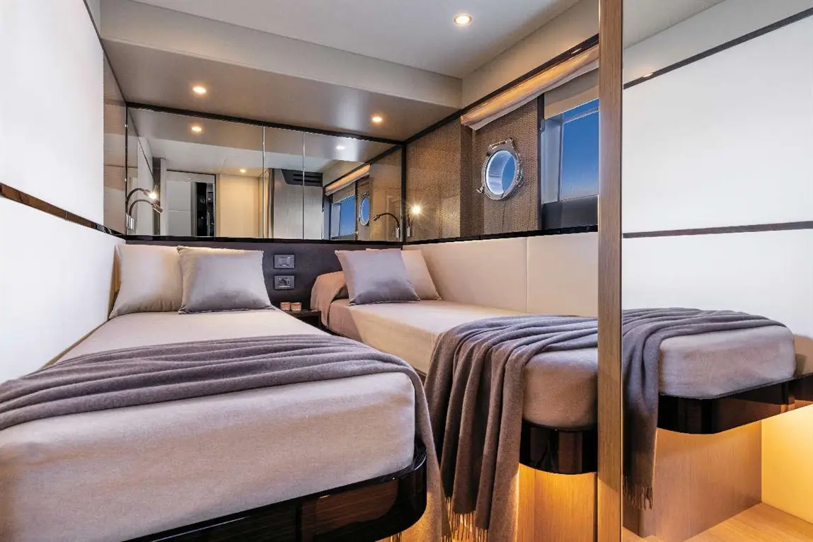 Modern twin bedroom with grey blankets and pillows, featuring a mirror wall and round porthole window.